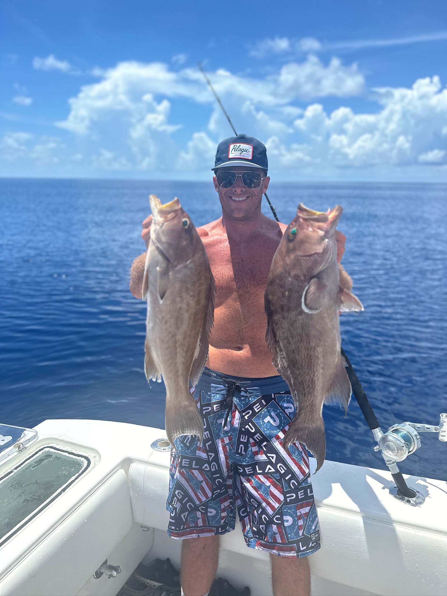 An angler with two grouper under a bluebird sky